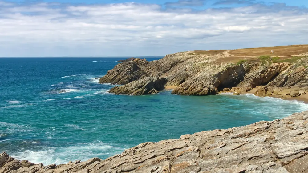 La côte sauvage : falaises de schiste, criques turquoise et lande rase sous un ciel de traîne