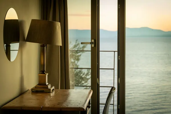 Lampe et bureau devant une porte-fenêtre ouverte sur la mer au couchant