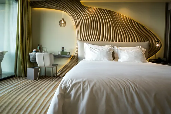 Chambre au grand lit blanc sous une tête de lit de bois cintré, en vagues