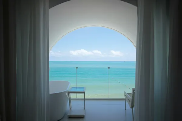 Baignoire îlot devant une grande fenêtre en arc ouverte sur la mer turquoise