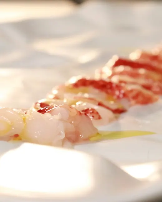 Tranches de homard cru sur une assiette blanche, un filet d’huile d’olive