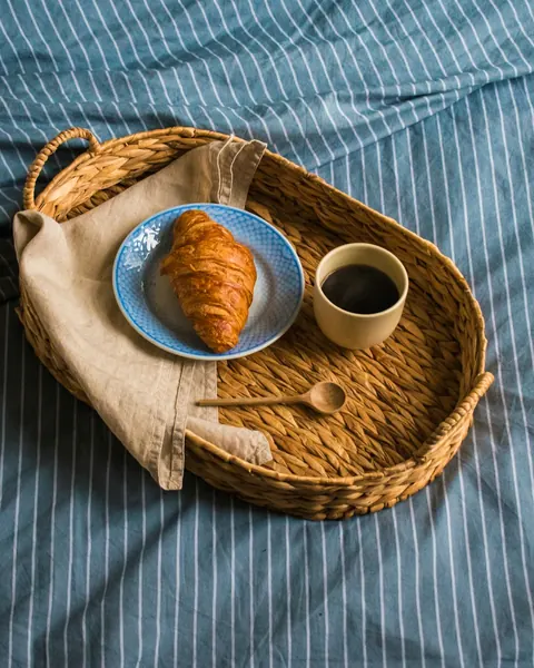 Plateau d’osier sur un drap rayé bleu : croissant et tasse de café